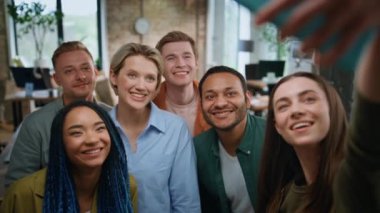 Şirket takımı, modern ofiste selfie çekiyor. Yakın çekim. Mutlu iş arkadaşları akıllı telefon fotoğraflarına bakıp gülüyorlar. Grup çok ırklı meslektaşları cep telefonuyla fotoğraf çekerken gülümsüyor.