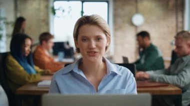 Video toplantısında yönetici karşılaması ofisteki iş yerinde takım arkadaşlarıyla yakın çekim. Laptop kamerasına gülümseyen neşeli iş kadını. Kız asistan kadın CEO 'nun dikkatini çevrimiçi aramadan dağıtıyor