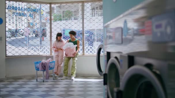 爱夫妻聊天洗衣房 十几岁的女孩在公共洗衣店洗衣服 两个不同的朋友在自助服务室聊天 聊得很开心 青少年恋爱关系概念 — 图库视频影像