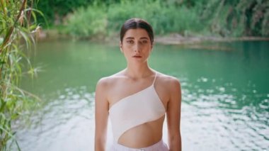 Serene modeli mavi su pozu veriyor. Beyaz mayo giyiyor. Yakın plan. Rahat, çekici bir kadın, turkuaz gölde duruyor, vahşi ormanın yakınında. Güzel bayan gölde yalnız dinleniyor.