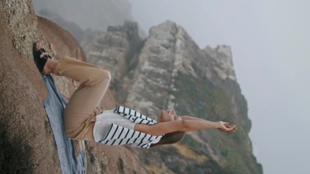 一个女人在暑假垂直伸展着海崖 平静的观望大海 沉思海滨野餐的生活 宁静美丽的女孩独自躺在岩石顶上放松 和平的生活方式 — 图库视频影像