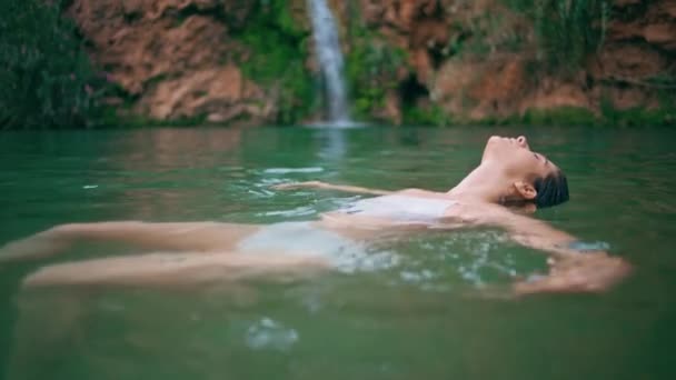 アクティビティを楽しむトランキルガールエメラルドグリーンウォータークローズアップ 一人で泳ぐリラックスした女性 荒野湾で魅惑的に髪に触れるカメラを見ている肖像感覚の女性 — ストック動画