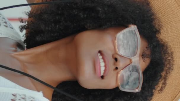 非裔美国人在海滩特写处享受阳光 在海滨 戴着太阳镜帽的垂直时髦卷曲的女孩休息了一下 微笑的游客整个暑假都在垂直拍摄 浪漫的情绪概念 — 图库视频影像