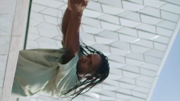 嘻哈男子跳舞街垂直特写 时髦的舞者独自在露天排练 在抽象建筑附近练习新舞蹈的黑人头发表演者 非裔美国人舞蹈课 — 图库视频影像