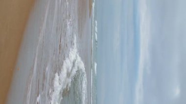 Dalgalar kasvetli bir günde okyanus kıyılarını yıkıyor. Huzurlu zen, meditasyon için uygun bir yer. Sakin deniz suyu bulutlu gökyüzünün altında boş kumlu sahile sıçrıyor. Dikey olarak sakin deniz manzarası kıyı şeridi.