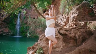 Kayalık sahilde yoga egzersizi yapan rahat bir kadın. Güneşli bir günde el ele tutuşan dikkatli bir genç kız. Sıska kadın kollarını güzel tropikal doğayla esnetiyor. Sağlık hizmeti kavramı