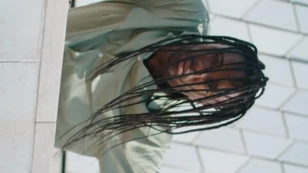 ドレッドロックは抽象的な壁の垂直の肖像画を踊る男を踊る 地区のコンクリートビルに触れる黒い髪の男 アフリカ系アメリカ人のダンサーが現代のテクニックを即興 カメラを見ているパフォーマー — ストック動画