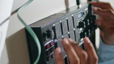 Erkek elleri konsol klavyesini dikey yakın plan kullanıyor. Afro-Amerikalı tanınmayan ses yapımcısı hafif dairede şarkı karıştırıyor. Çağdaş müzik yaratmak için bilinmeyen kahverengi deri DJ 'i düğmelere basıyor