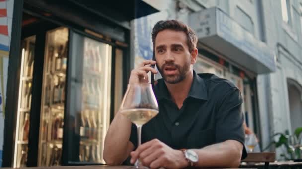 通りのバーで 携帯電話を呼んでる 市のオープンエアカフェで会話をしながらワイングラスを保持している男にひげをかけられた アルコールで一人で仕事をした後リラックスしたカジュアルビジネスマン — ストック動画