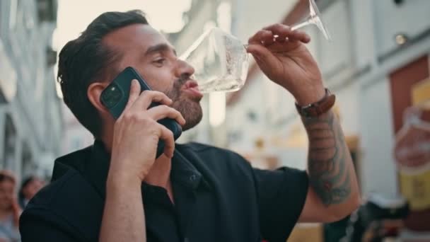 留胡子的家伙喝着酒杯 在街上咖啡馆的特写镜头前打电话来 西班牙裔中年男子在露天酒吧边喝酒边讲手机 有信心的商人在周末使用智能手机 — 图库视频影像