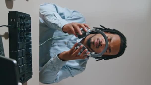 一个带耳机的自由人在公寓里做垂直特写 让音乐制作人思考满桌的设备 严重的非洲裔美国人安排家工作室工作 职业介绍和职业 — 图库视频影像