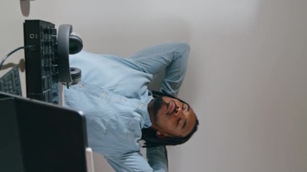 松驰的男人坐在扶手椅上垂直变焦 打哈欠的音乐制作人尝试在灯光下集中精神 非裔美国人自由撰稿人在远程录音室录制电子音轨 职业概念 — 图库视频影像