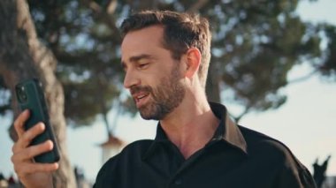 Green Plaza 'da kendine güvenen adam çevrimiçi konferansı. Şehir vatandaşı konuşuyor, cep telefonu kamerası yaz parkında duruyor. Videochat 'ta konuşan şık turist açık havada sohbetin tadını çıkarıyor. 