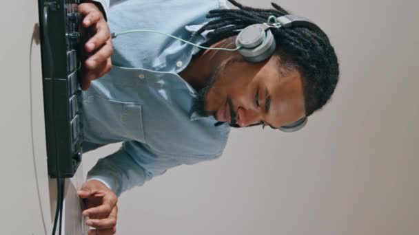 耳机男使用控制器公寓垂直特写 非裔美国人音乐制作人摸Midi键盘看笔记本电脑 编曲人在家里的录音室里用音响设备创作歌曲 — 图库视频影像