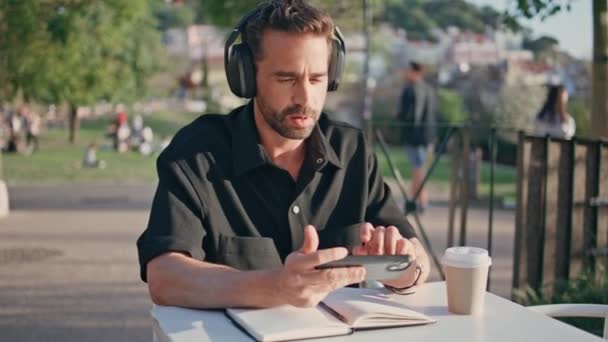 Headphones Homem Digitando Celular Desfrutando Música Mesa Parque Perto Produtor — Vídeo de Stock