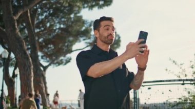 Şehir gözlem güvertesinde video bloğu kaydeden mutlu adam cep telefonuyla konuşuyor. Gülümseyen İspanyol blogcu sosyal medyada görüntülü konuşma yapıyor. Rahat, şık bir turist cep telefonu kamerasıyla konuşuyor. 