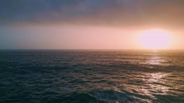 Güzel okyanus dalgaları üzerinde inanılmaz turuncu kıyı günbatımı havadan görünüyor. Sakin deniz manzarasında bulutlu bulutlu bir gökyüzü. Deniz suyu yavaş çekimde gün batımını yansıtıyor. Akşam deniz manzarası