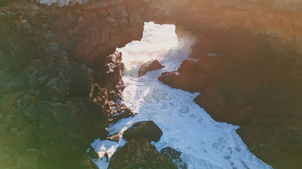 粗糙的海洋岩石海岸被泡沫般的气泡水缓慢地冲刷着 无人机发射了令人兴奋的 阳光灿烂的海浪海景 汹涌的海浪在火山岩上溅落 强烈的海浪冲破悬崖 — 图库照片