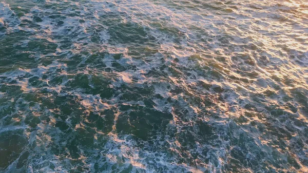 ゴールデンサンセットライトでドローンビュー海水面 夜の日差しを反映した深海を発見 高い沿岸岩の下で転がる波は白い泡の遅い動きを作ります 海洋の風景 — ストック写真
