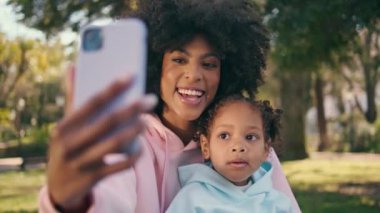 Anne çocuk telefonda güzel yeşil çayırda fotoğraf çekiyor. Yakın plan. Gülümseyen Afro-Amerikalı kadın modern akıllı telefon kullanarak küçük kızıyla selfie çekiyor. Teknoloji konsepti.