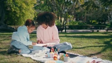 Güzel, yeşil çimenli, güneşli bir hafta sonunda piknik yapan yaratıcı aile çizimi. Afro-Amerikan annesi, sanattan hoşlanan tatlı bir kızla kağıt üzerinde resim yapıyor. Neşeli anne çocuk resim yapıyor..