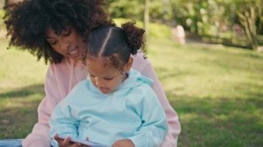 Afro-amerikan aile telefonlarını güneşli doğada otururken yaklaş. Mutlu kaygısız kadın küçük çocuklara yeşil çimlerde rahatça oyun oynuyor. Dışarıda animasyon videosu izleyen sevimli bir çocuk.