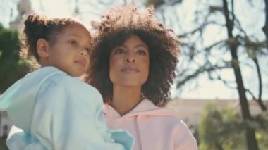 Güneş parkında yürüyen kızı taşıyan Afrikalı Amerikalı bir anne. Doğada küçük bir kızla gezmekten hoşlanan çekici, mutlu bir kadın. Tasasız aile hafta sonu birlikte. Annelik mutluluğu.