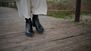 Autumn boots walking wooden path closeup. Calm traveler legs strolling walkway on gloomy day. Unrecognized casual woman tourist explore enjoying quiet place. Lonely female relax looking inspiration