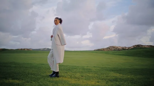 stock image Calm woman walking field on spring vacation. Beautiful serene model look camera going green grass at cloudy sky. Pensive african american take break enjoy solitude outdoors. Peaceful meadow landscape