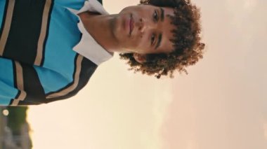 Şehrin akşam resminde elinde paten tutan şık bir öğrenci. Günbatımı dikey videosunda tek başına kameraya bakan genç bir adam. Güler yüzlü kaykaycı şehir merkezinde poz veriyor. Çağdaş yaşam tarzı kavramı.