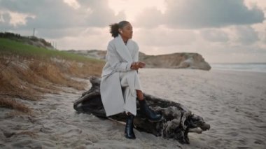 Güz plajında zarif kadınlar kulaklık takar. Huzurlu siyah saçlı kız okyanus kıyısında dinleniyor bulutlu bir günde dalgaları seyrediyor. Güzel Afro-Amerikan Yöneticisi telefonla konuşuyor. Tatilde danışmanlık yap.