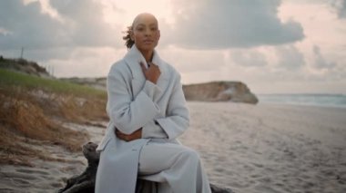 Okyanus sahilini yalnız düşünen ciddi bir kadın. Hüsrana uğramış Afro-Amerikan pozu sabah soğuk kıyıda dinleniyor. Siyah saçlı, üzgün model dışarıda sorunları düşünüyor. Yalnız düşünceli kadın.
