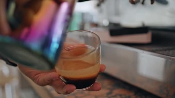 在餐馆里准备新鲜咖啡的手关门了 不知名的咖啡师在美味的浓缩咖啡中倒入热牛奶 制成美味的美式拿铁咖啡 咖啡工人手挽着旋转的玻璃杯咖啡因饮料 — 图库视频影像