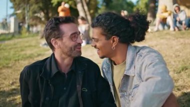 Mutlu eşcinsel erkek arkadaşlar güneşli çimlerde oturup kaygısız hafta sonunun tadını çıkarırlar. İki melez homoseksüel adam yaz parkında dinleniyor. Neşeli eşcinsel çift tatilde eğleniyor..