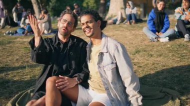 Eşcinsellerin hafta sonlarını parkta battaniyeye yakın oturarak geçirmesi. Mutlu homoseksüel aşıklar birlikte bir şeyler arıyor. Gülümseyen lgbt partnerleri romantik buluşmada güneşli doğanın tadını çıkarırlar..