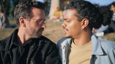 Parktaki yeşil çimlerde oturan homoseksüel aile güneşli bir günde kapanıyor. Rahatlamış, etnik çeşitliliğe sahip iki adam güzel çimlerde birlikte takılıyor. Mutlu lgbtq partnerleri doğada romantik bir hafta sonu geçiriyor..