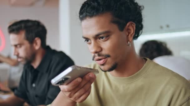 拉丁裔男子坐在自助餐厅里记录语音讯息 一个英俊的年轻人在酒吧里用扩音器说话 现代智能手机休息 通过手机应用发送音频短信的小胡子自由职业者 — 图库视频影像