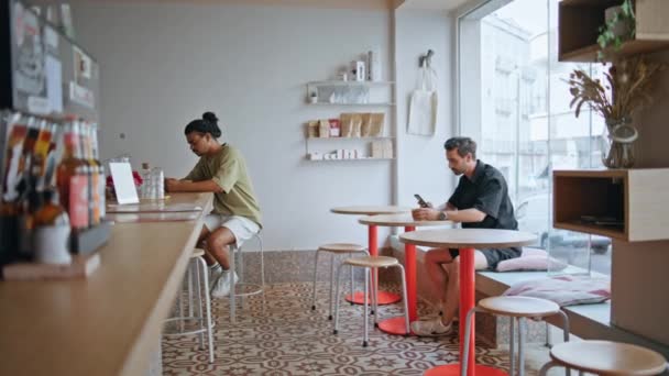 两个咖啡店的顾客分别坐在舒适的机构内部 多种族游客自助餐厅享用美味的咖啡因饮料 情侣们在咖啡馆里用智能手机放松一下 — 图库视频影像