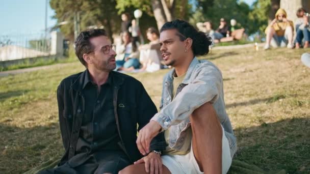 两个同性恋者一起坐在草地上晒太阳 共度周末 在浪漫的约会中 快乐的多种族同性恋伴侣谈论着共同的梦想 宽松的大夫妇享受公园的自然 变性人之爱 — 图库视频影像