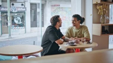 Rahat homoseksüel erkek arkadaşlar küçük, rahat kafeteryada buluşuyorlar. Kafe masasında oturmuş gülümseyen ve birlikte eğlenen çok ırklı eşcinsel çift. Romantik çeşitlilikte homoseksüel iki erkek kaygısız buluşmanın tadını çıkarır..