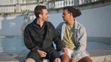 Romantik eşcinseller kenar mahalle meydanında rahatlıyor. Neşeli gülümseyerek konuşan pozitif melez lgbt ortakları açık havada romantik buluşmaların tadını çıkarın. Mutlu homoseksüel aşıklar birlikte aşk mutluluğu hissediyorlar..