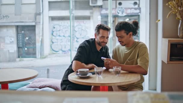 Гей Пара Выглядит Смартфон Сидя Маленький Столик Ресторан Молодой Латиноамериканец — стоковое видео