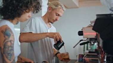 Cafe çalışanları kahve hazırlıyor. Modern kahvecinin mutfağını kapatın. Sıcak espressoya süt döken genç barista nefis latte yapıyor. Mutfakta çalışan deneyimli kafeterya çalışanları.