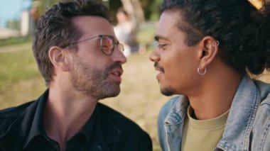 Alışılmadık oryantasyon portresi yapan bir çift erkek yaz doğasında öpüşüyor. Mutlu eşcinsel çoklu etnik partnerler yeşil çimen parkında oturmuş konuşuyor. Sevimli eşcinsel aşıklar romantik bir hafta sonunda aşktan zevk alırlar.