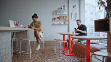 İki adam, kafenin içinde akıllı telefonlarla rahat rahat oturuyor. Kafeterya ziyaretçileri rahat ahşap masalarda dinleniyor cep telefonu ekranlarına bakıyor. İki kafe müşterisi içeride espresso içiyor..
