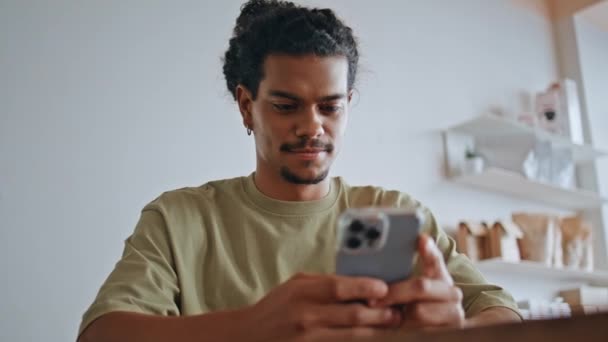 ブラジル人男性がコーヒーハウスに座っている携帯電話をテキストで送信する スマートフォン画面を見ているラテン系の男性は 読書メッセージに不満を持っています ムスタシュ カーリー ヒップスター 携帯電話でソーシャルメディアをスクロール — ストック動画
