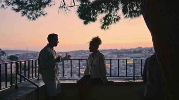 恋人们在夕阳西下聊天的轮廓 在浪漫的约会中 男人举着酒杯给女朋友讲故事 一对快乐的多民族夫妇在城景享受无忧无虑的夜晚 — 图库视频影像