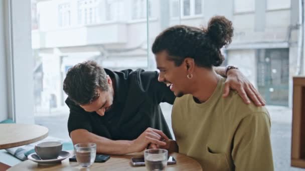 快乐的同性伴侣拥抱坐在舒适的咖啡店近旁 两个多种族的男人在咖啡馆里开浪漫约会的玩笑 快乐的同性恋者一起享受周末 Lgbt关系概念 — 图库视频影像