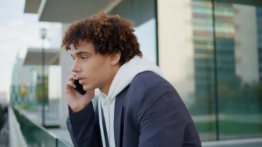 Cam terasta cep telefonuyla konuşan ciddi bir genç. Modern mimaride telefonla konuşan odaklanmış bir adam. Binanın arka planında genç bir adam konuşuyor. Kıvırcık hippi akıllı telefonla konuşuyor.