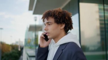 Genç adam cam balkonda cep telefonuyla konuşuyor. Modern mimari geçmişinde telefon dili konuşan kıvırcık adam. Elinde cep telefonu olan yakışıklı bir genç terasta sakince konuşuyor.